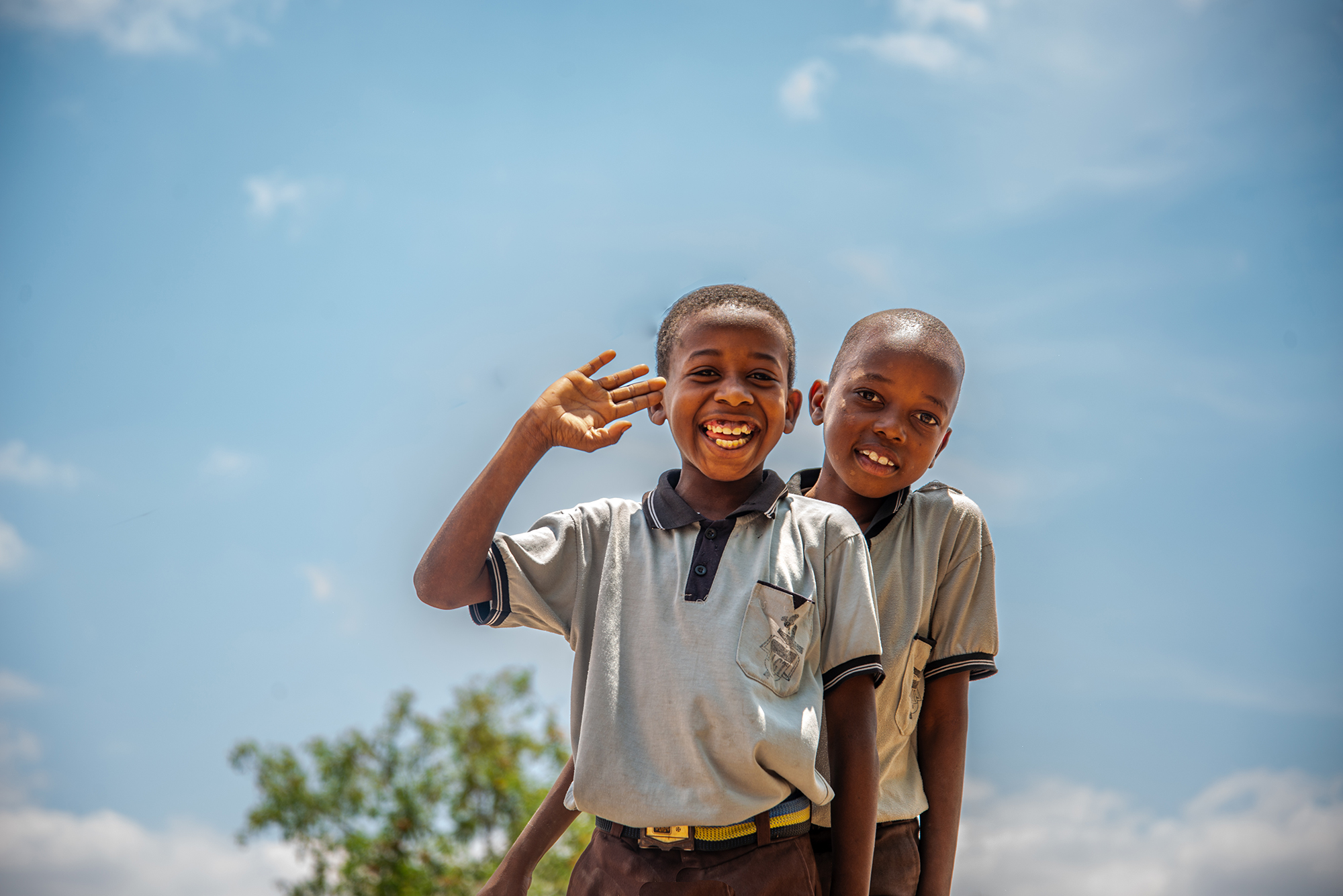 Two young boys smile for the camera while one waves.